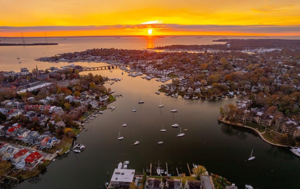 Experience the best things to do in Rock Hall MD in the fall like this aerial shot of a harbor and Chesapeake Bay at sunset, showing fall leaves, boats, and water.